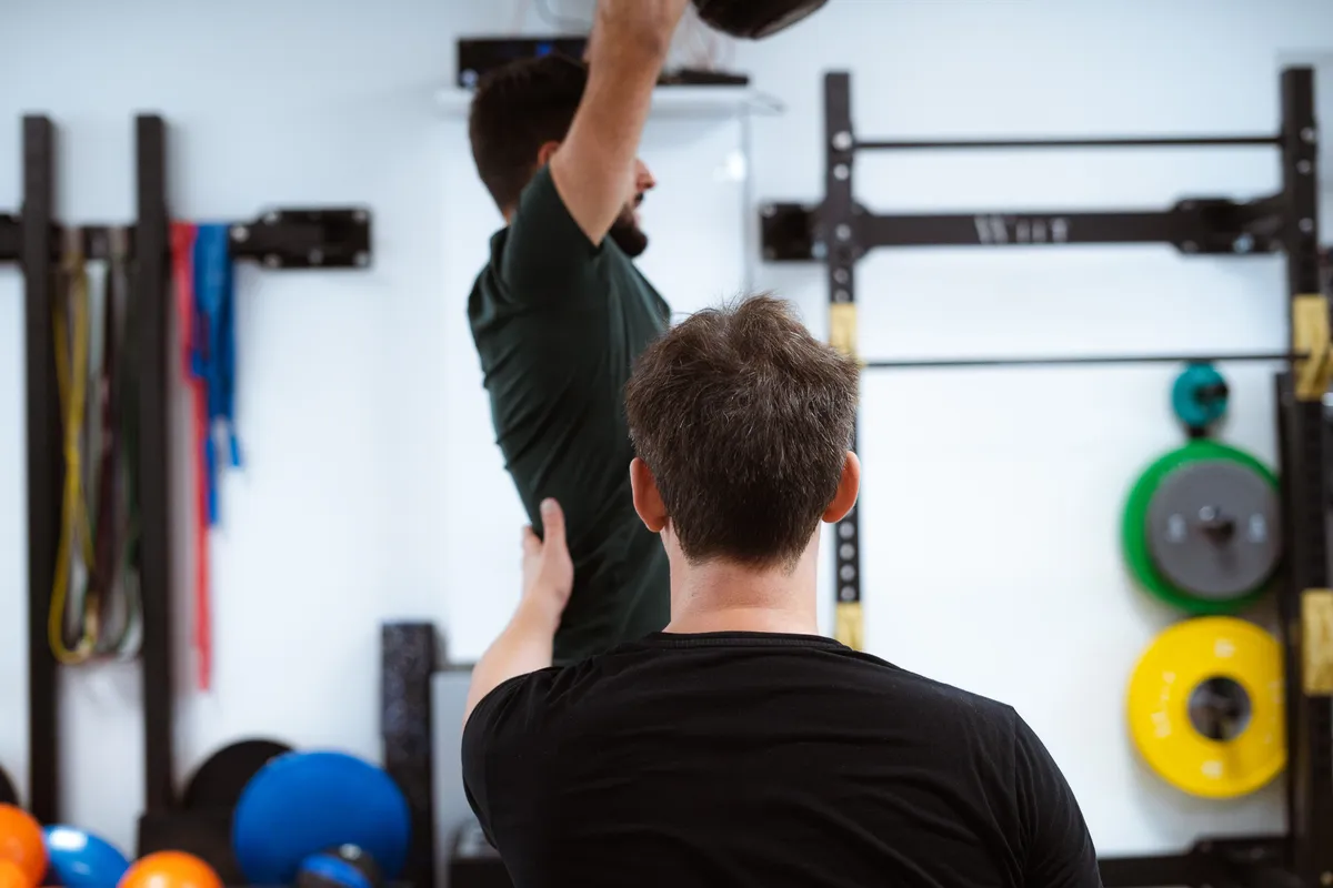 Un homme montre un mouvement bras levé à un autre adhérent devant un rack de musculation