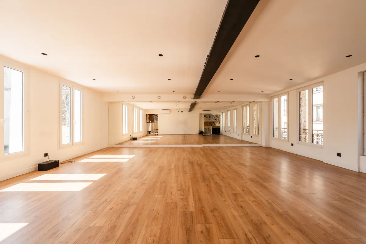Grand studio vide au parquet clair, hautes fenêtres, miroirs et poutre métallique apparente