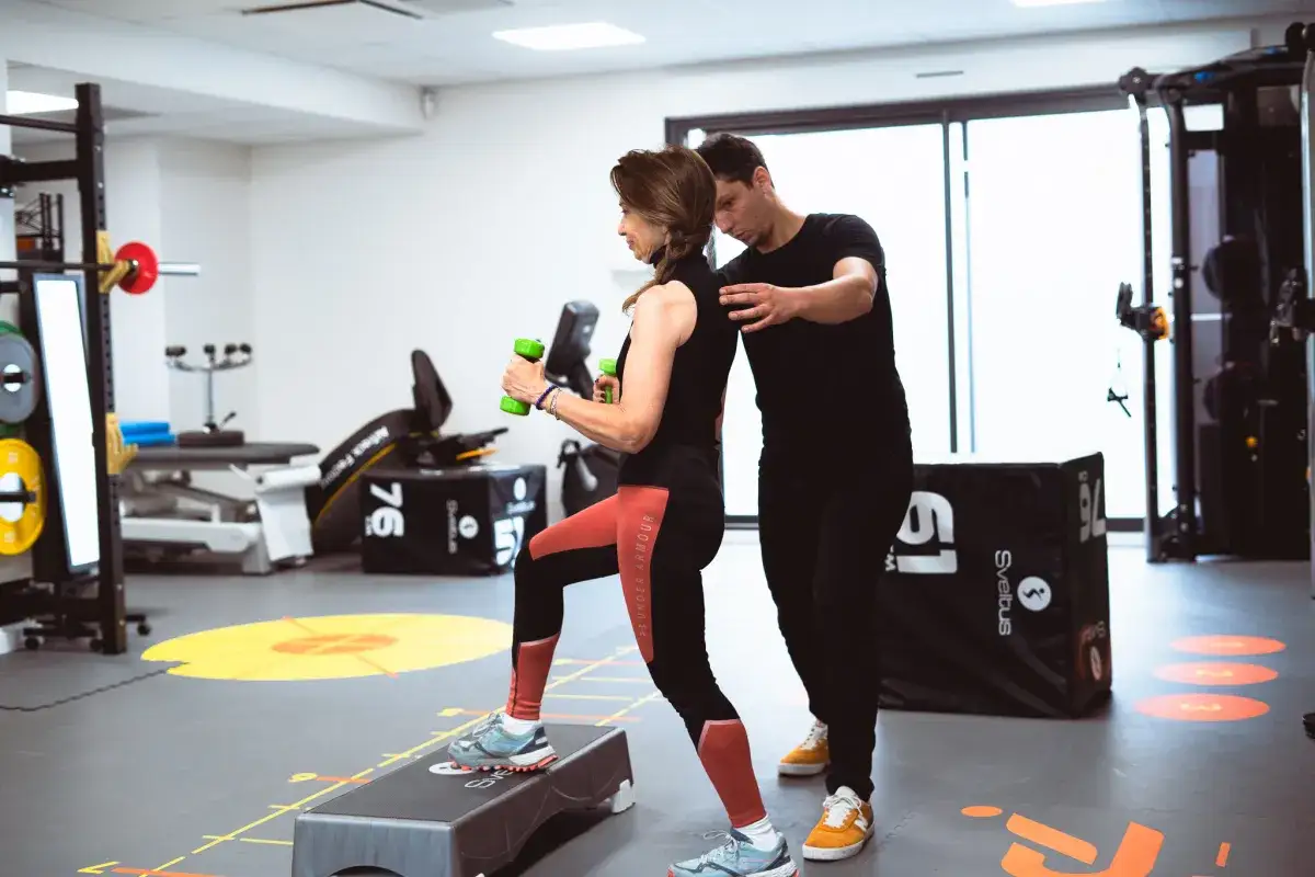 Coach guidant une adhérente lors d'un exercice de montée sur step avec haltères