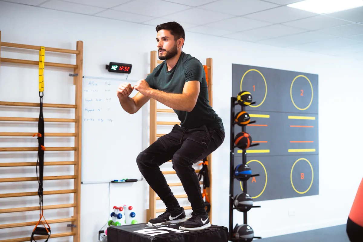 Adherente realisant un developpe epaules avec halteres assistee par un coach