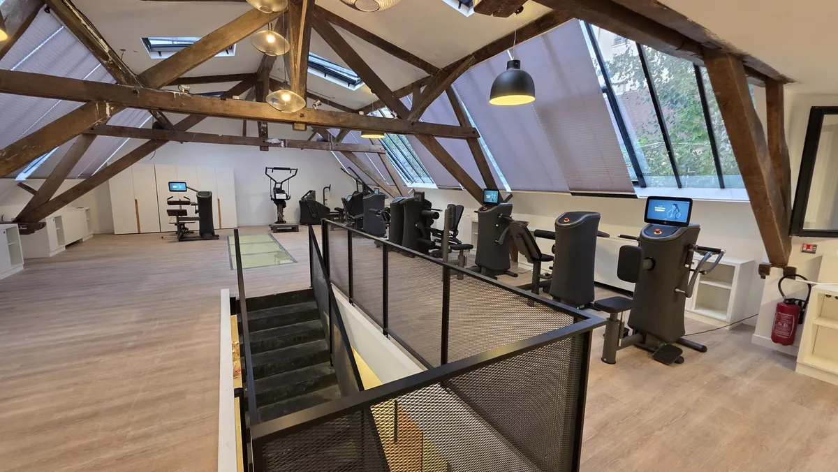 Rangée de machines eGym alignées sous la charpente en bois de la salle du Marais