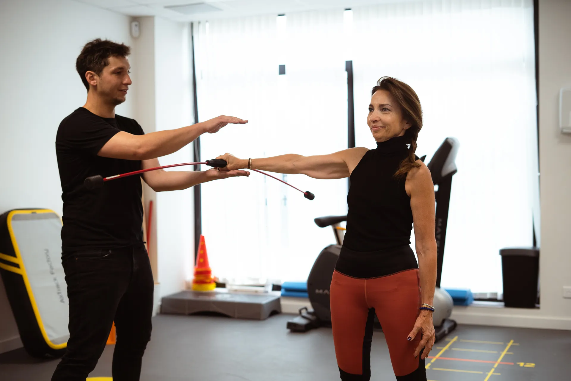 A physiotherapist guides a patient holding a red oscillating bar at arm's length