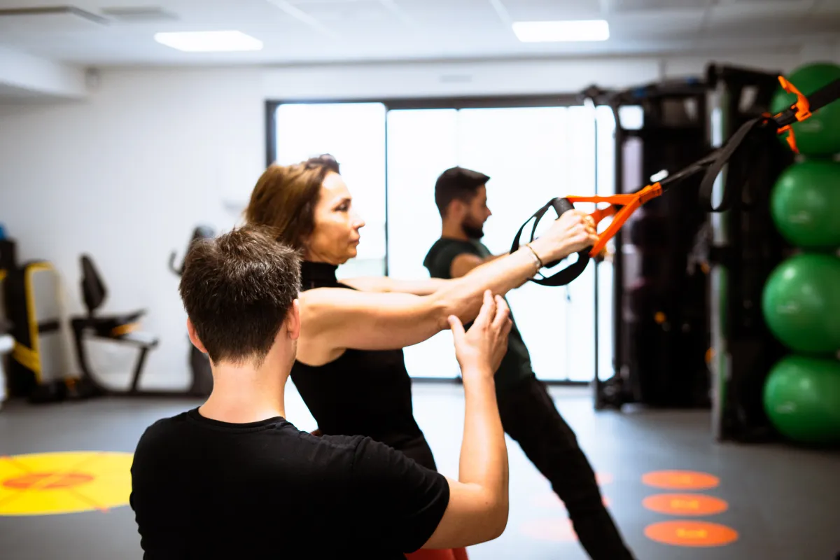 Une adhérente travaille sur sangles TRX, guidée par un coach qui corrige sa posture
